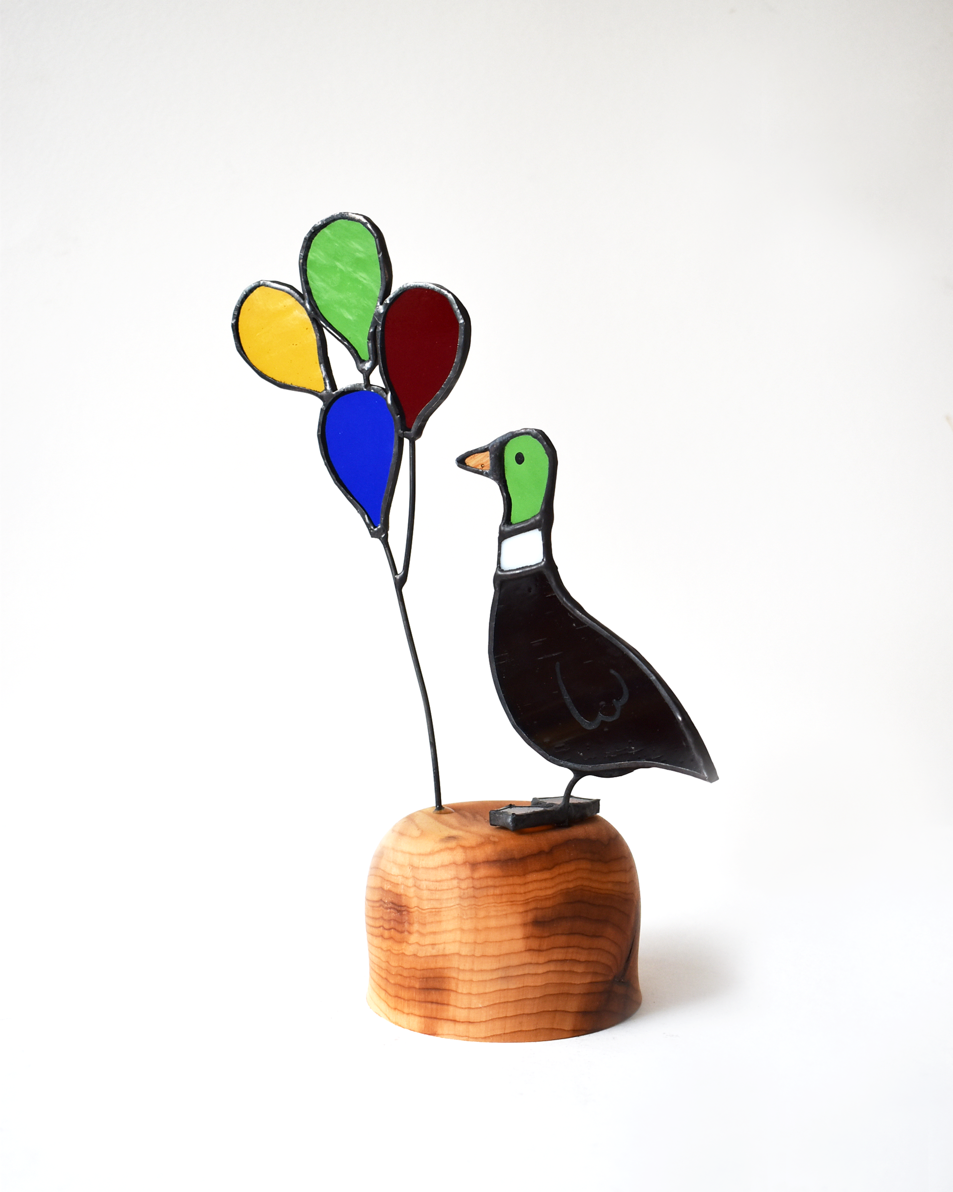 Decorative glass sculpture of a bird with colorful balloons on a wooden base against a white background