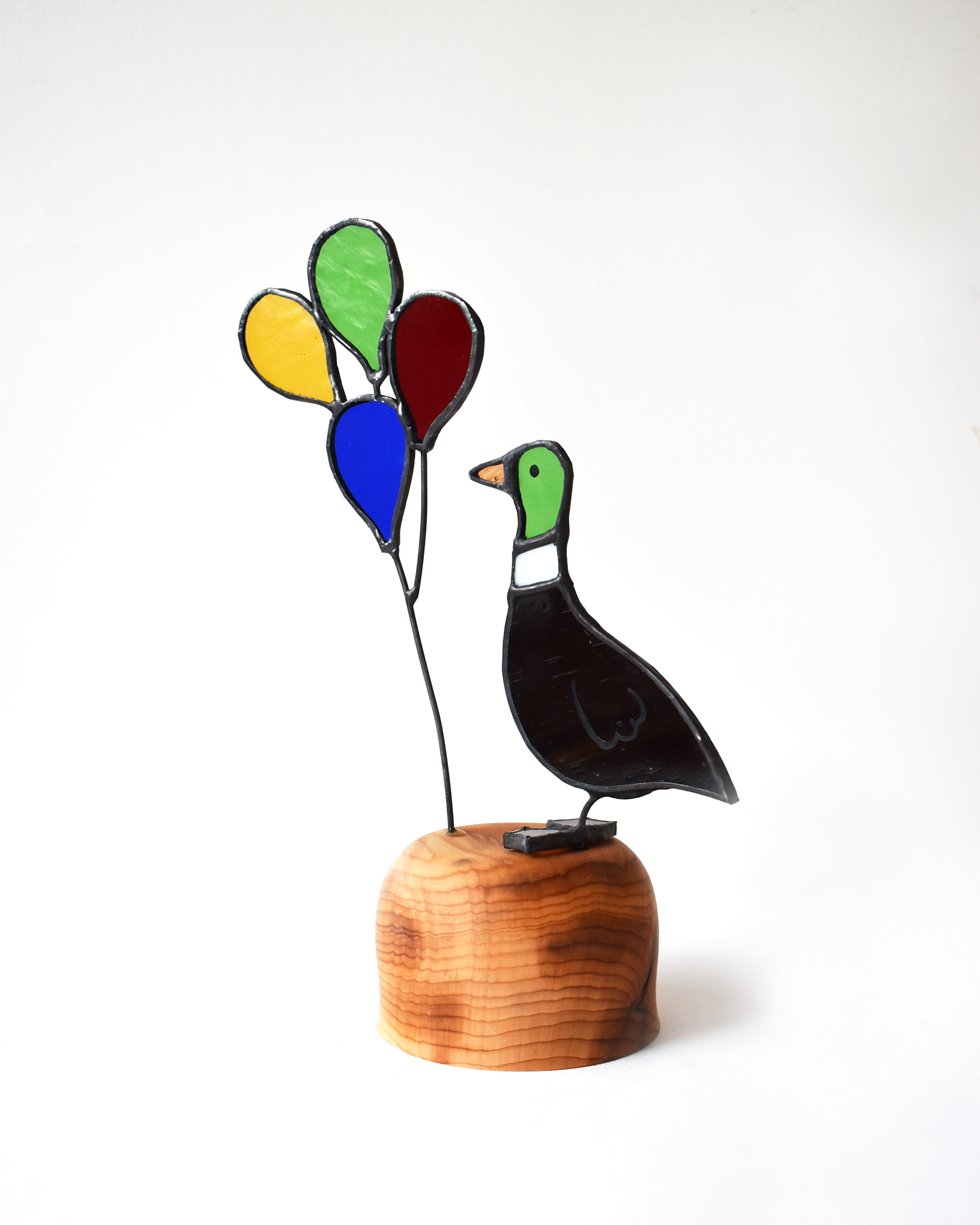 Decorative glass sculpture of a bird with colorful balloons on a wooden base against a white background