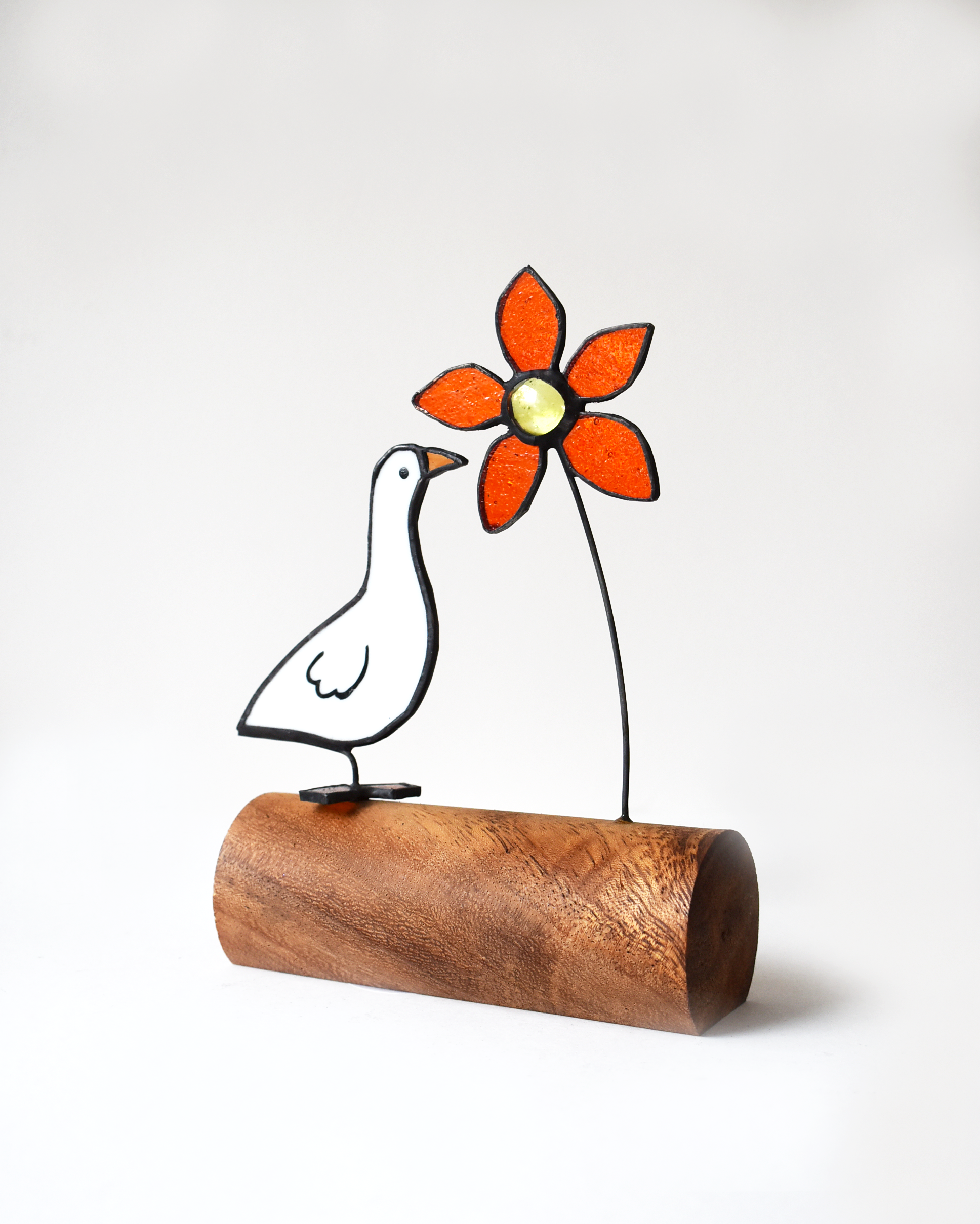 Decorative sculpture of a bird holding a flower on a wooden base against a white background