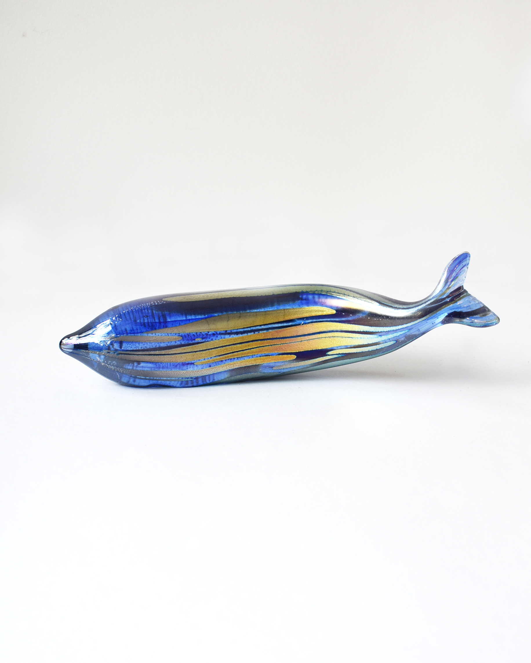 Glass sculpture of a fish with blue and yellow patterns on a white background
