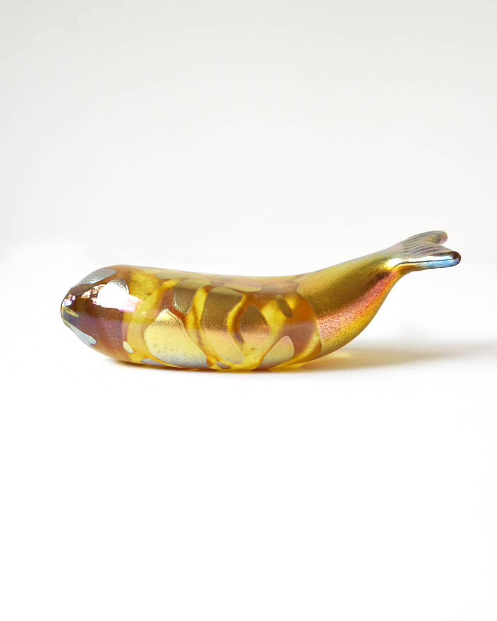 Glass sculpture of a fish with gold and brown colors on a white background
