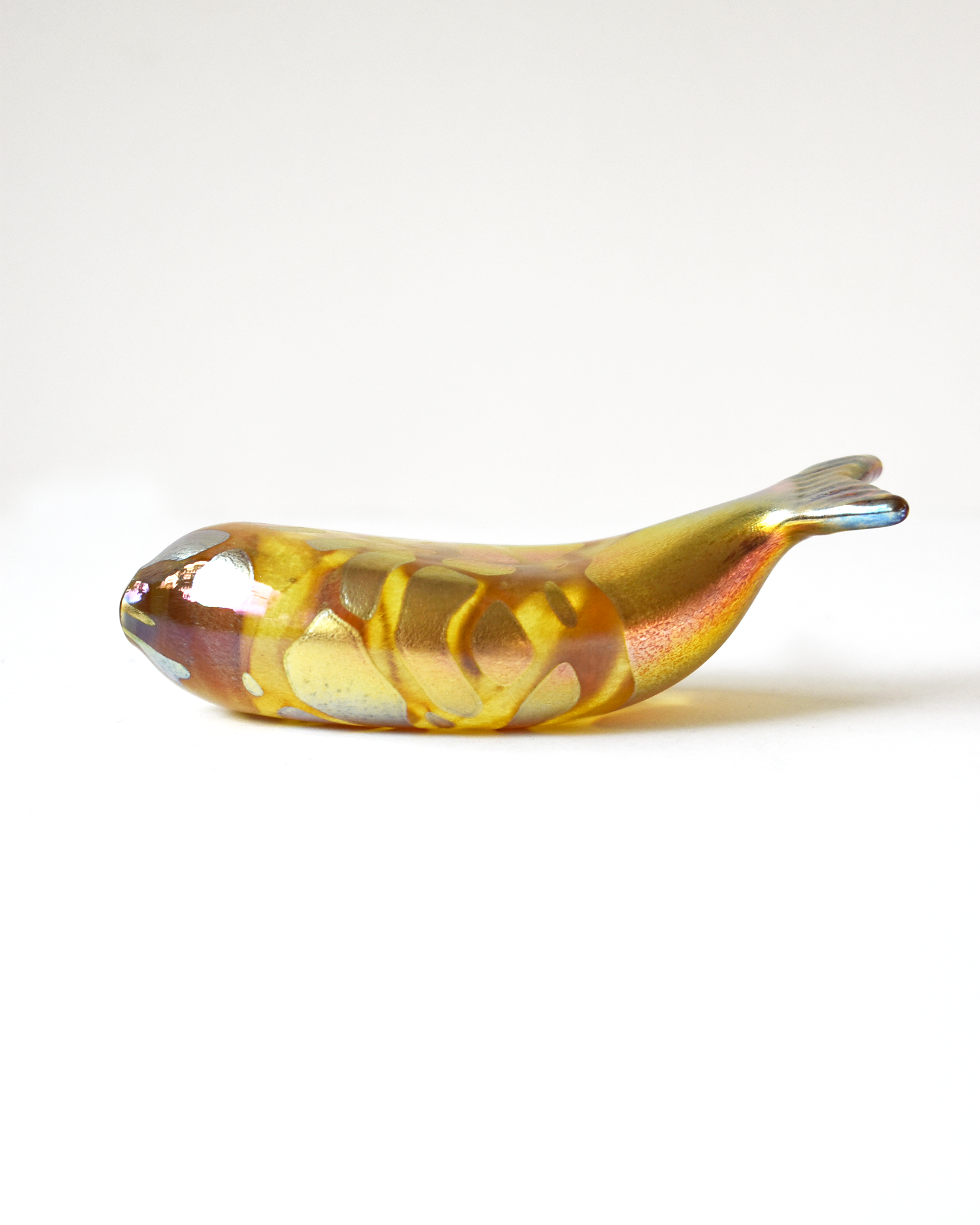 Glass sculpture of a fish with gold and brown colors on a white background