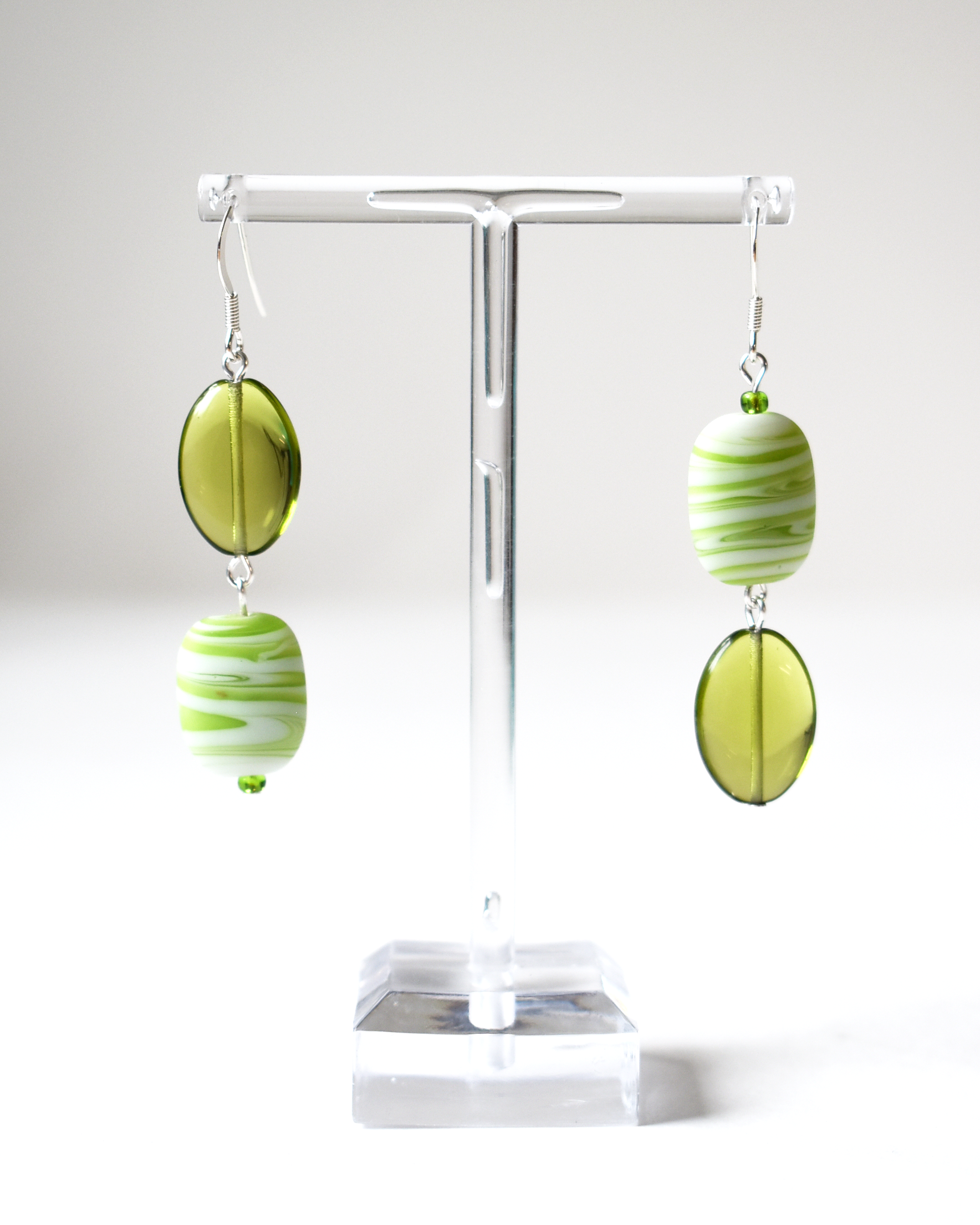 Green and white striped earrings on a white stand with a white background