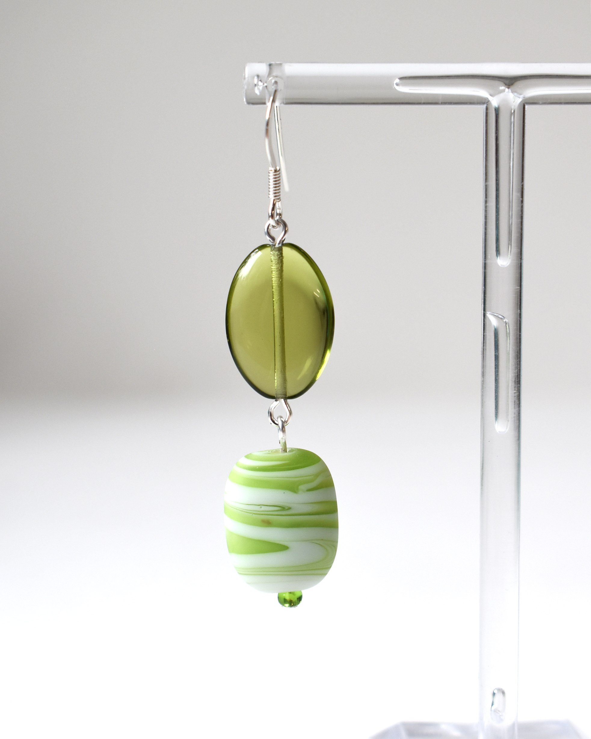 Green and white striped earrings on a clear stand against a white background