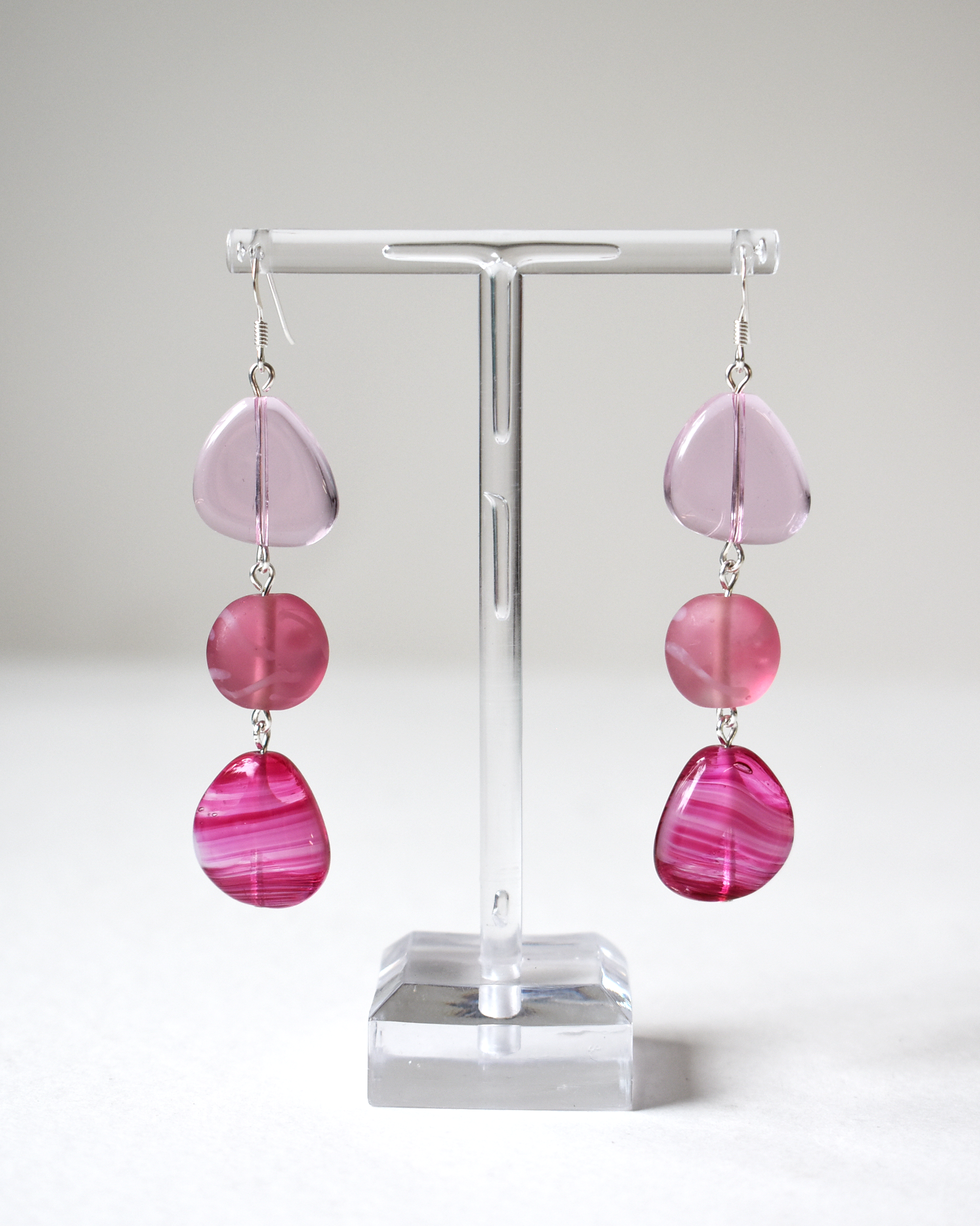 Pink teardrop earrings on a clear stand against a white background
