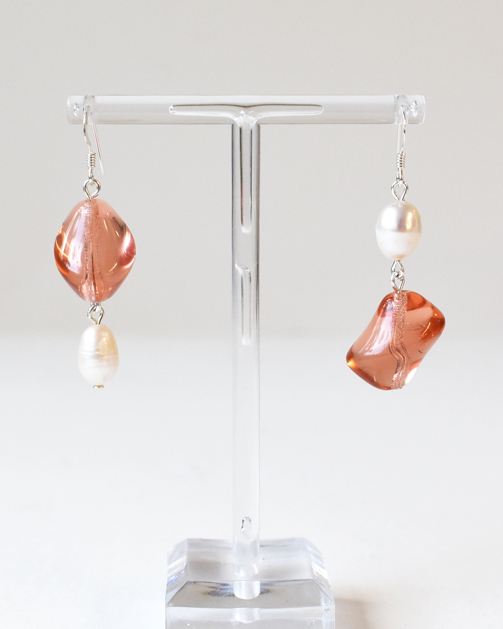 Pair of earrings with pink and white stones on a clear stand against a white background