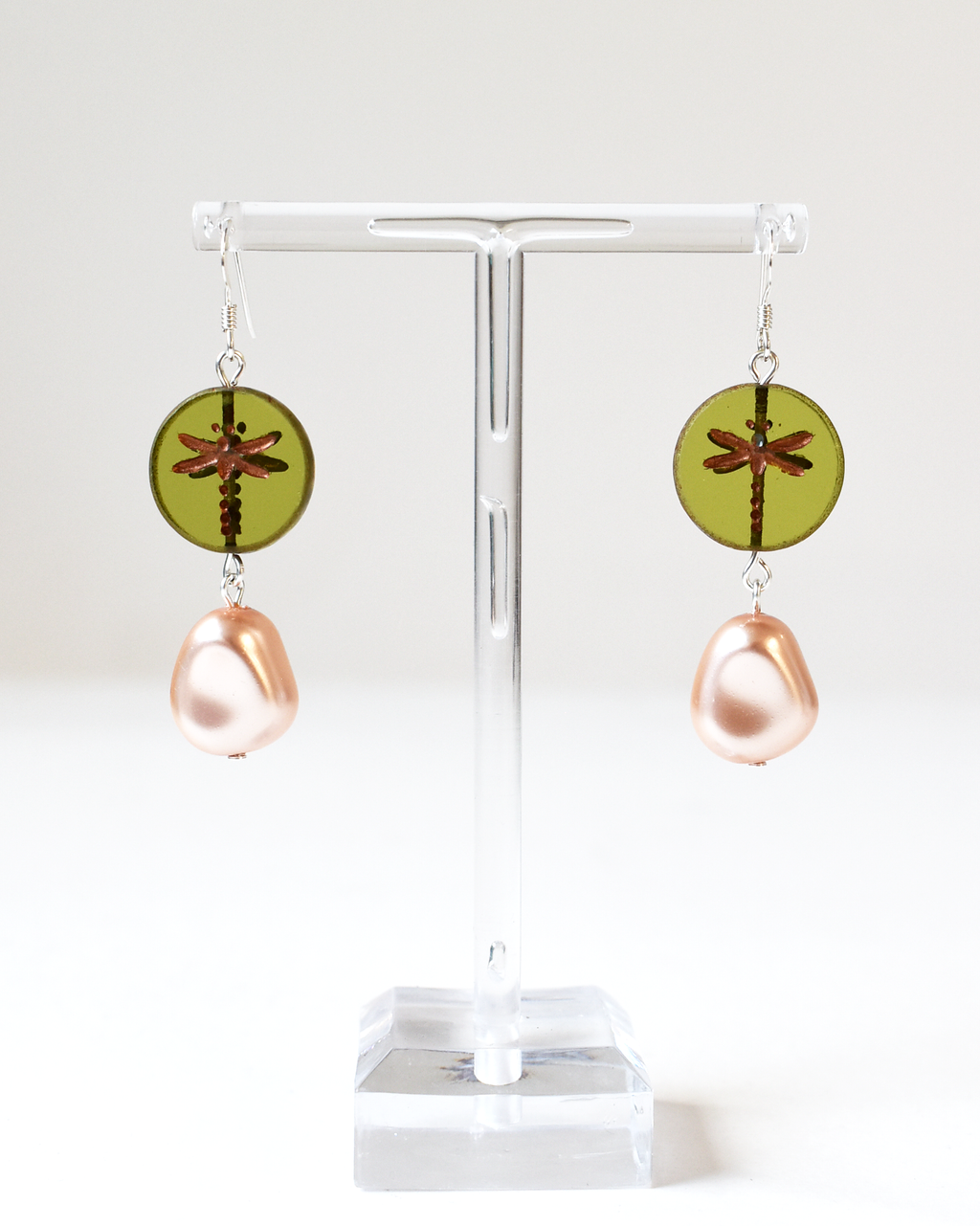 Pair of earrings with green circular and pink teardrop designs on a white stand.
