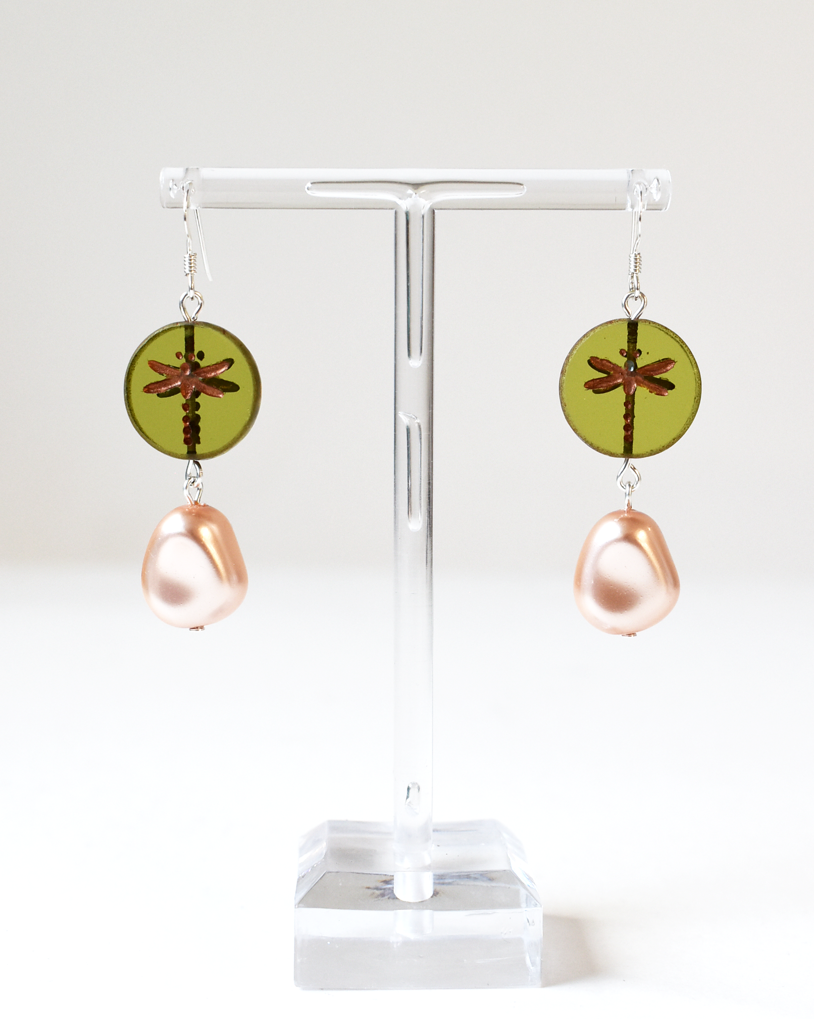 Pair of earrings with green circular and pink teardrop designs on a white stand.