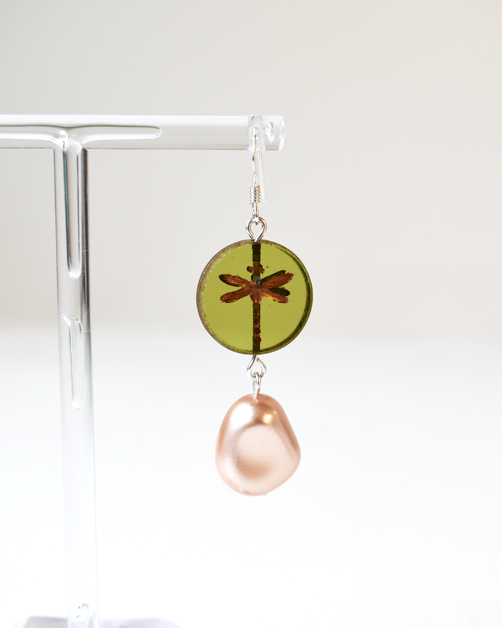 Earring with green round pendant and pink teardrop on a clear stand