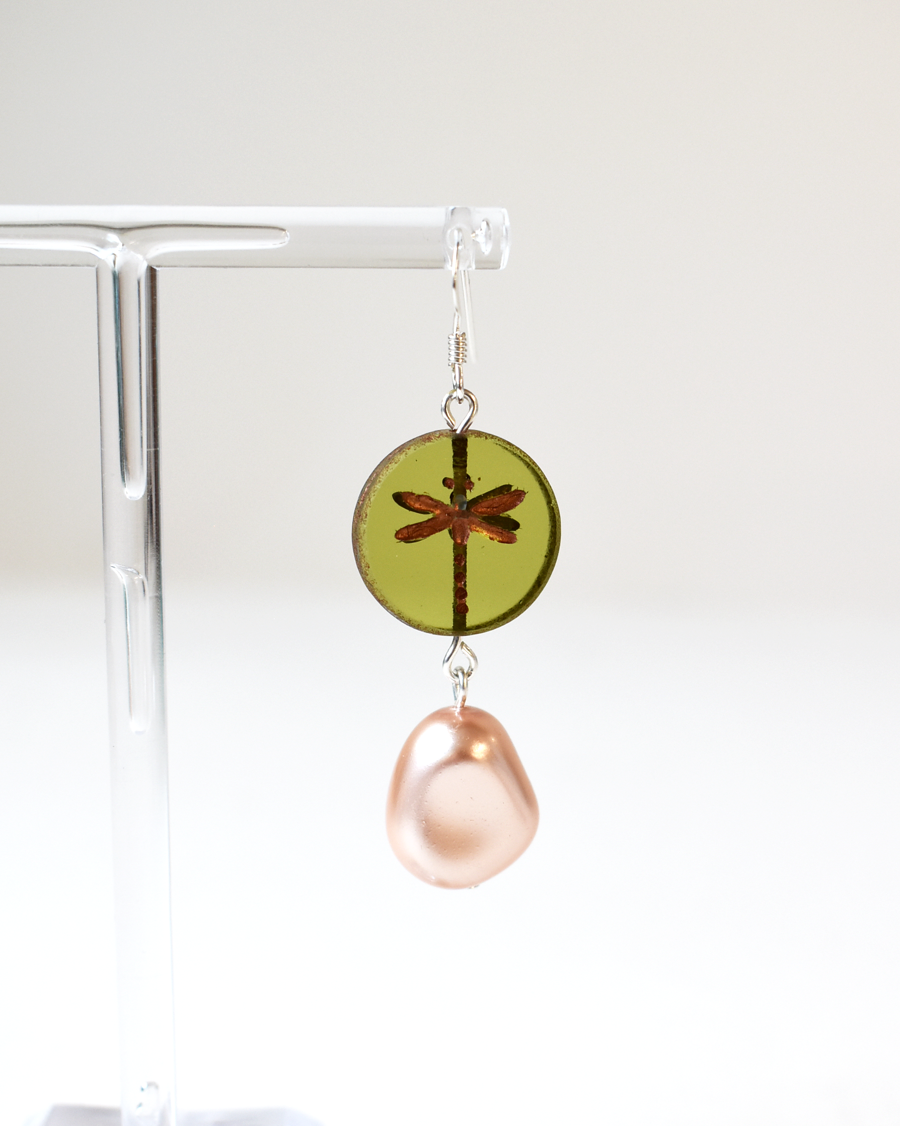 Earring with green round pendant and pink teardrop on a clear stand