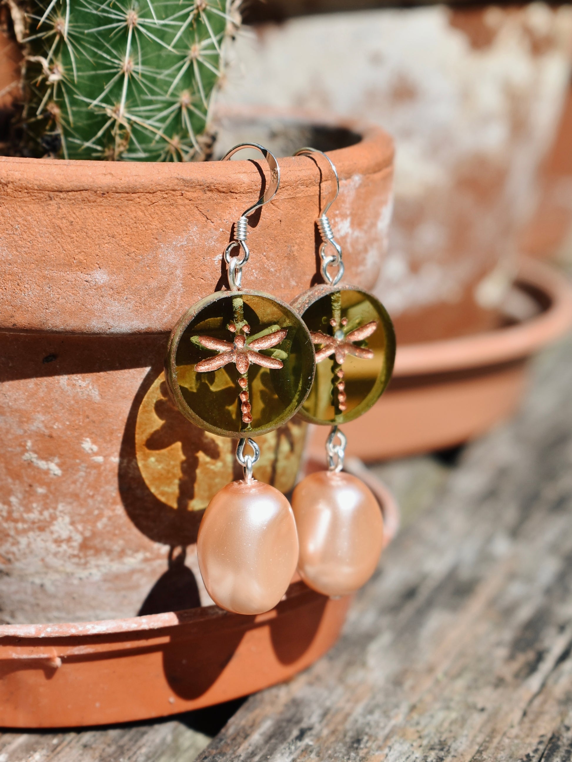 Gold dragonfly earrings with pink pearls on a wooden surface with a cactus in the background