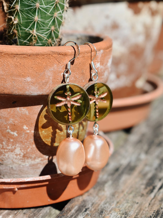 Gold dragonfly earrings with pink pearls on a wooden surface with a cactus in the background