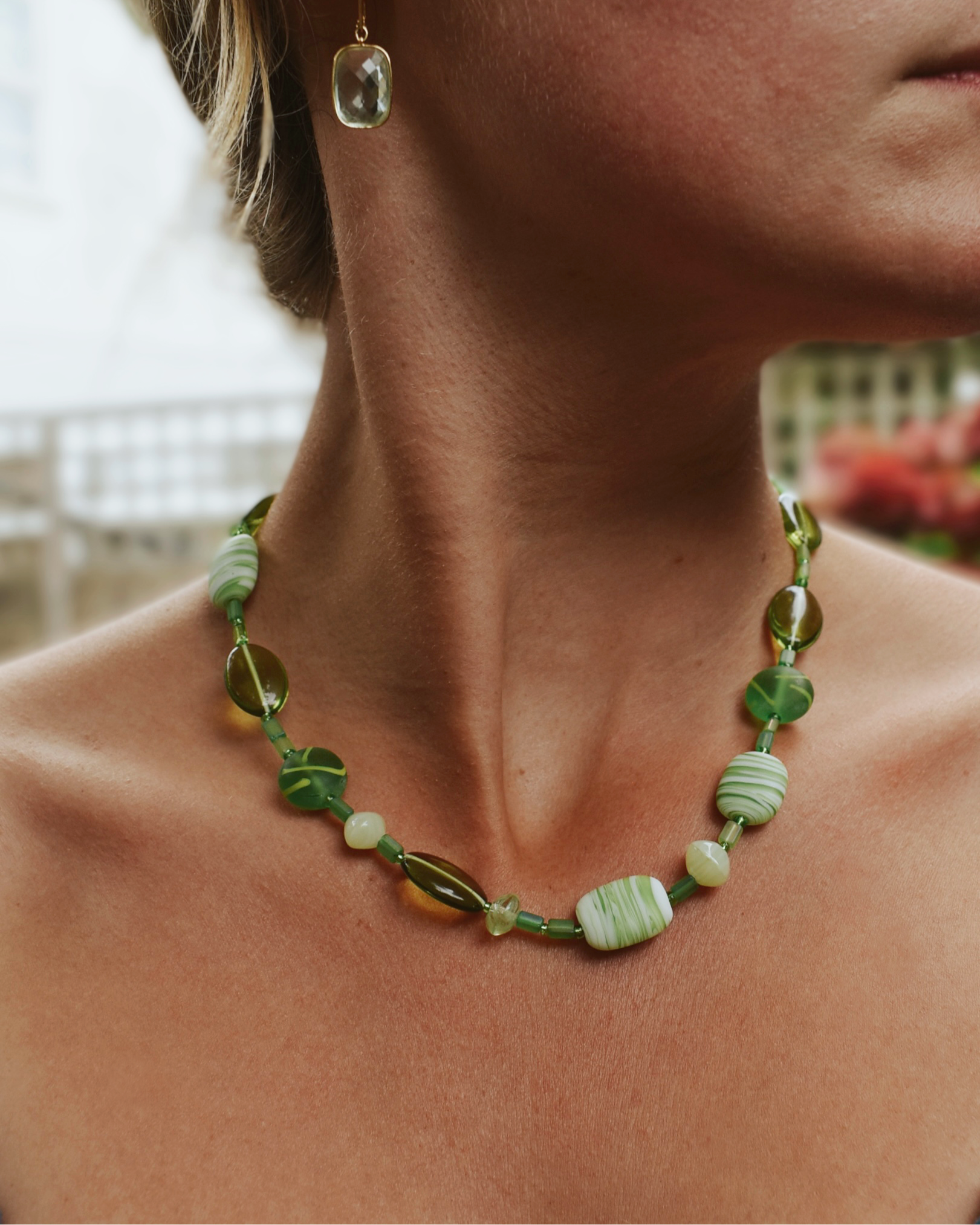 Close-up of a person wearing a green beaded necklace with a blurred background