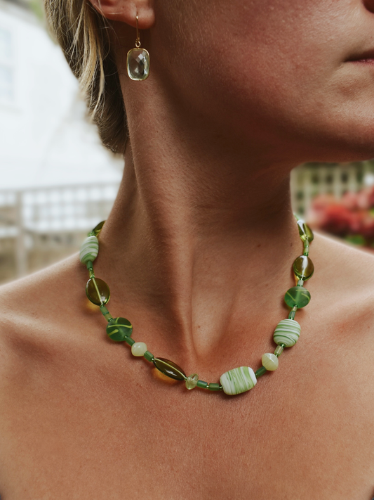 Close-up of a person wearing a green beaded necklace with a blurred background