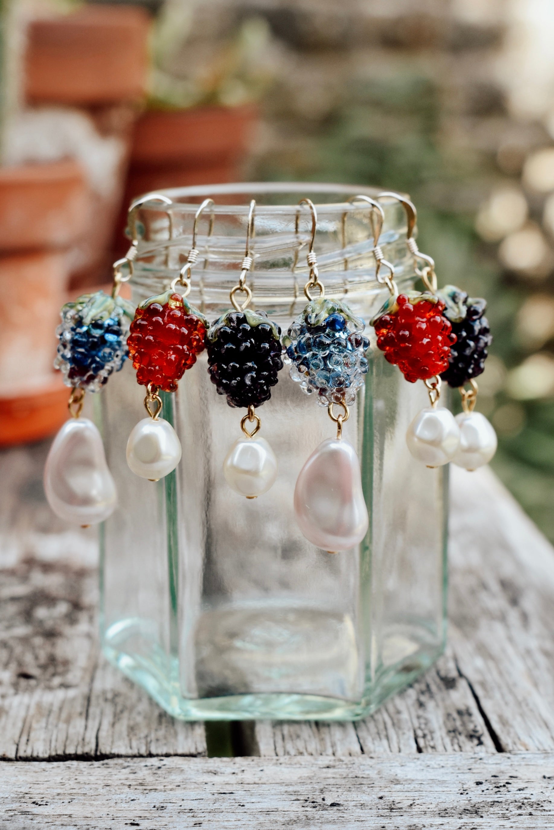 Jewelry set with colorful beads and pearls displayed in a glass jar on a wooden surface.