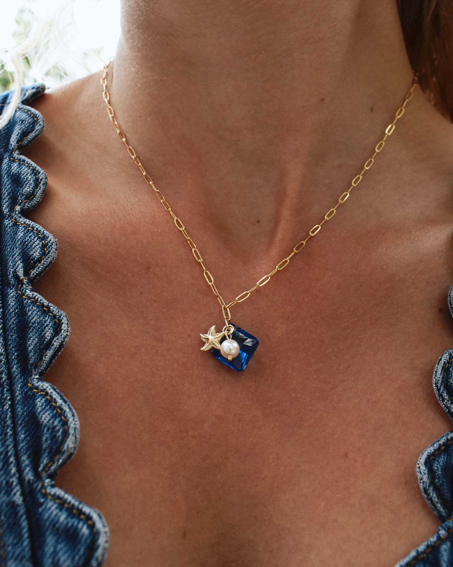Necklace with star and pearl pendant worn by a person in a blue top.