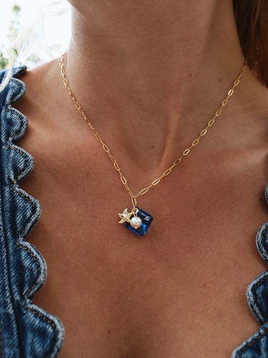 Necklace with star and pearl pendant worn by a person in a blue top.
